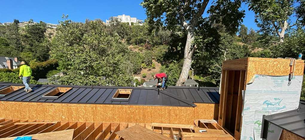 Two roofers installing metal panels across an active framed roof, featured on the Alhambra roofing page.