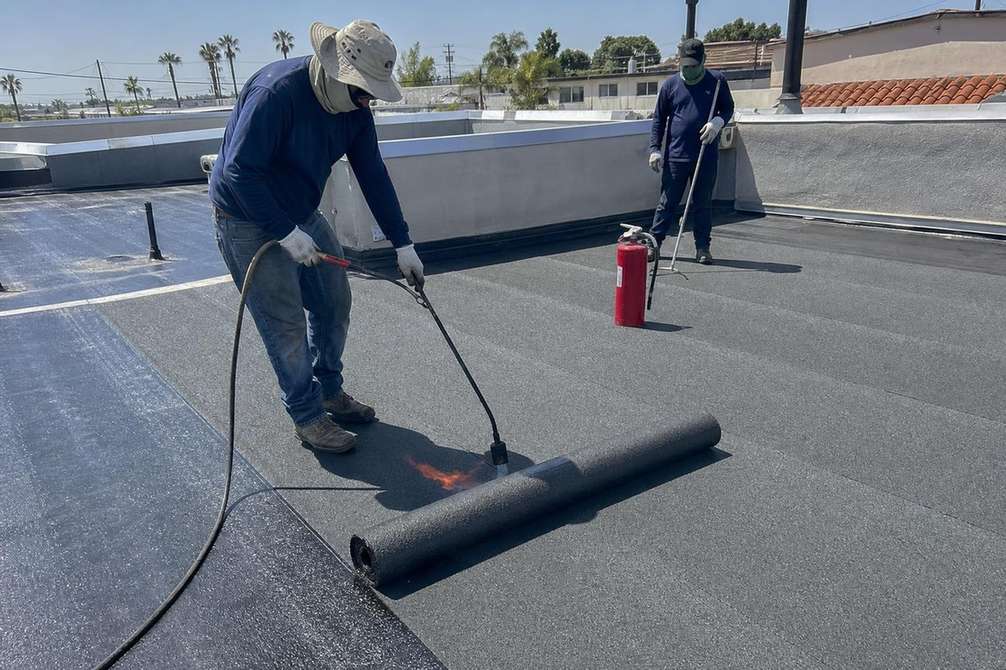 Roofers working across a low-slope roofing surface, featured on the Pasadena torch down roofing page.